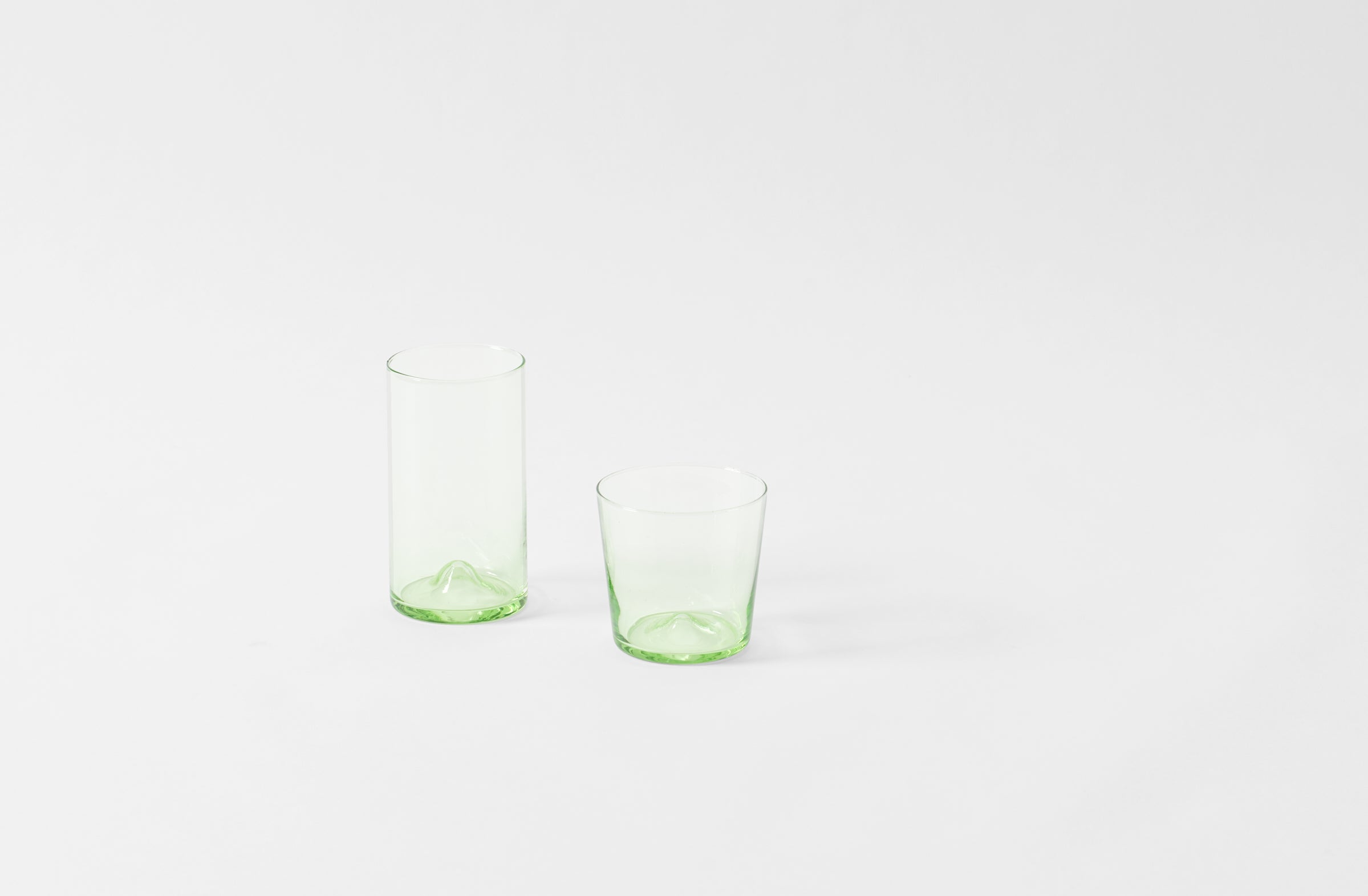 Two green glass tumblers on a white background. Default