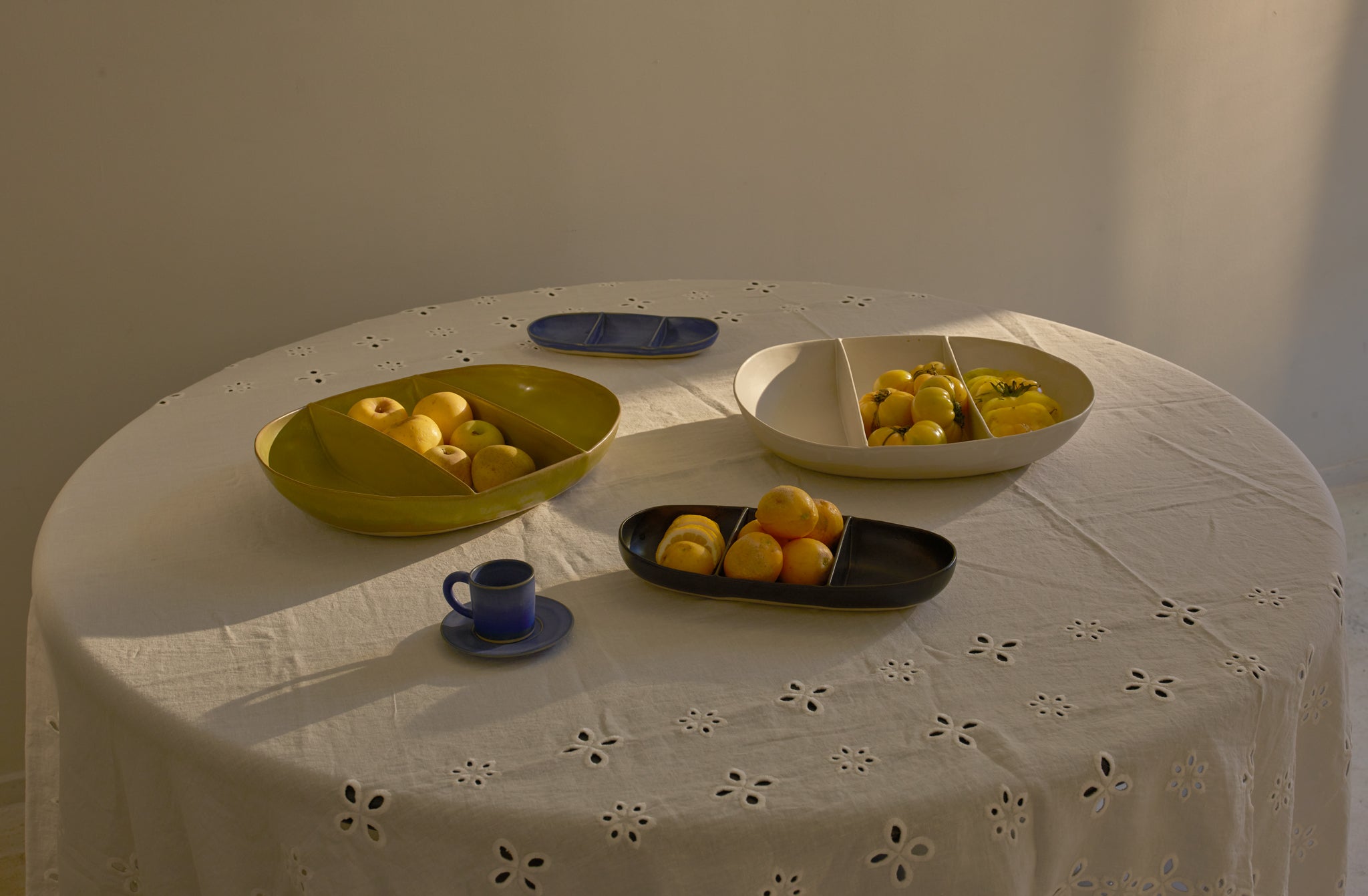 Large and small yellow-green indigo and white-beige Christiane Perrochon divided dishes with cheery yellow tomatoes and citrus on a round table covered with white Italian sangallo tablecloth.