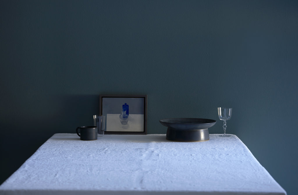 Christiane Perrochon grey blue cake stand and mug with Lobmeyr Poppea glass next to small Jason Line painting on table against blue grey wall. Default
