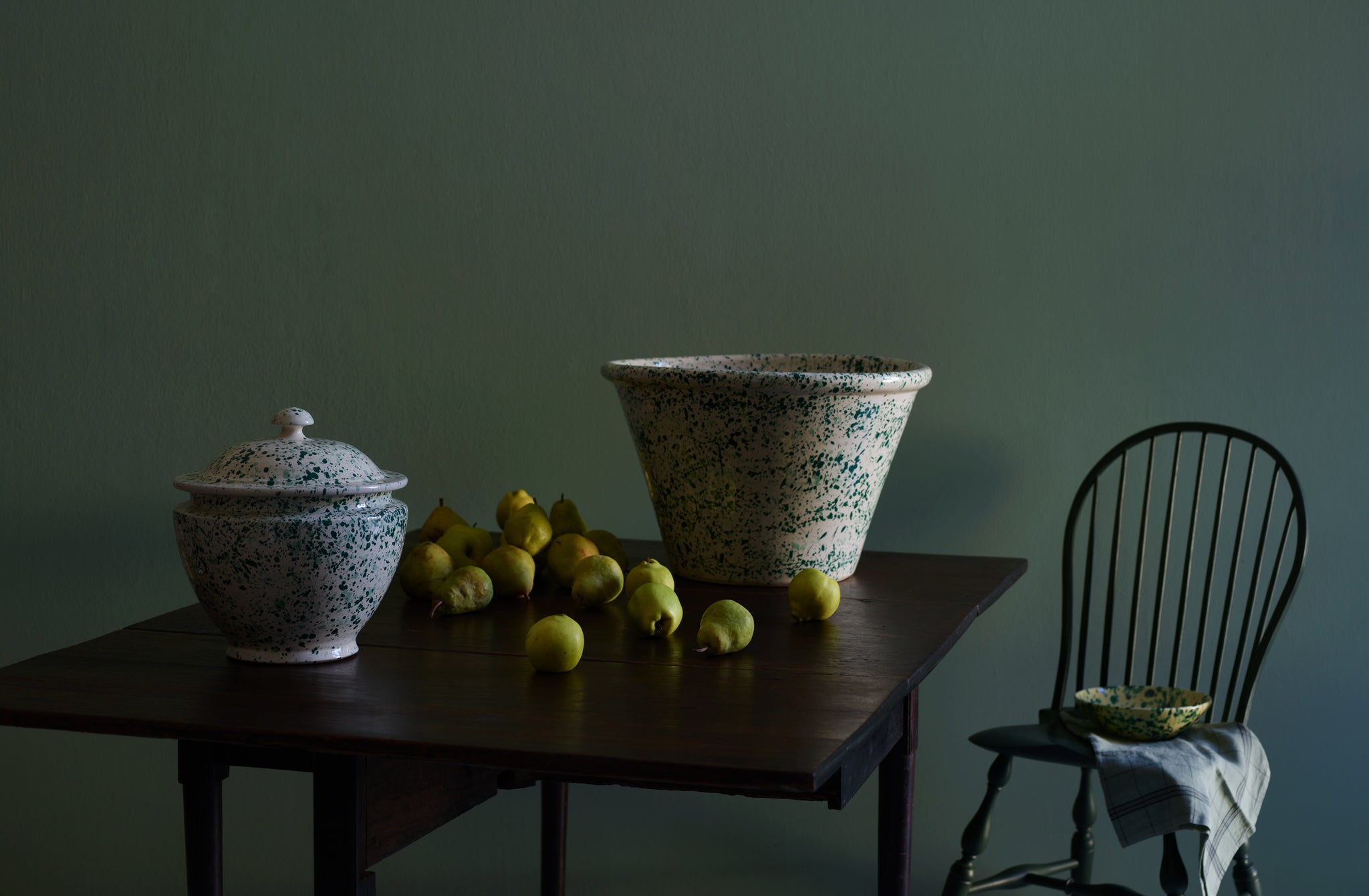 Double green MARCH splatterware extra large basin bowl and extra large soup tureen on antique 19th century Mallorca table with tumbling mound of green pears next to Sawyer Made hunter green side chair.