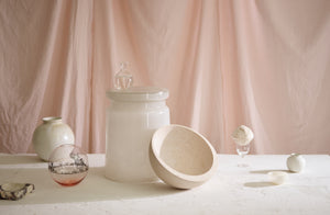 objects including a small onyx bowl set around a glass stool as a still life with a pink linen background