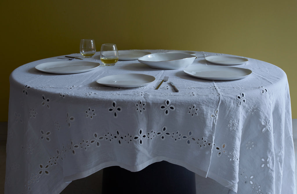 Molosco white dinnerware and serving bowl with gold rim set for entertaining on a Italian sangallo tablecloth against a gold green wall. Default
