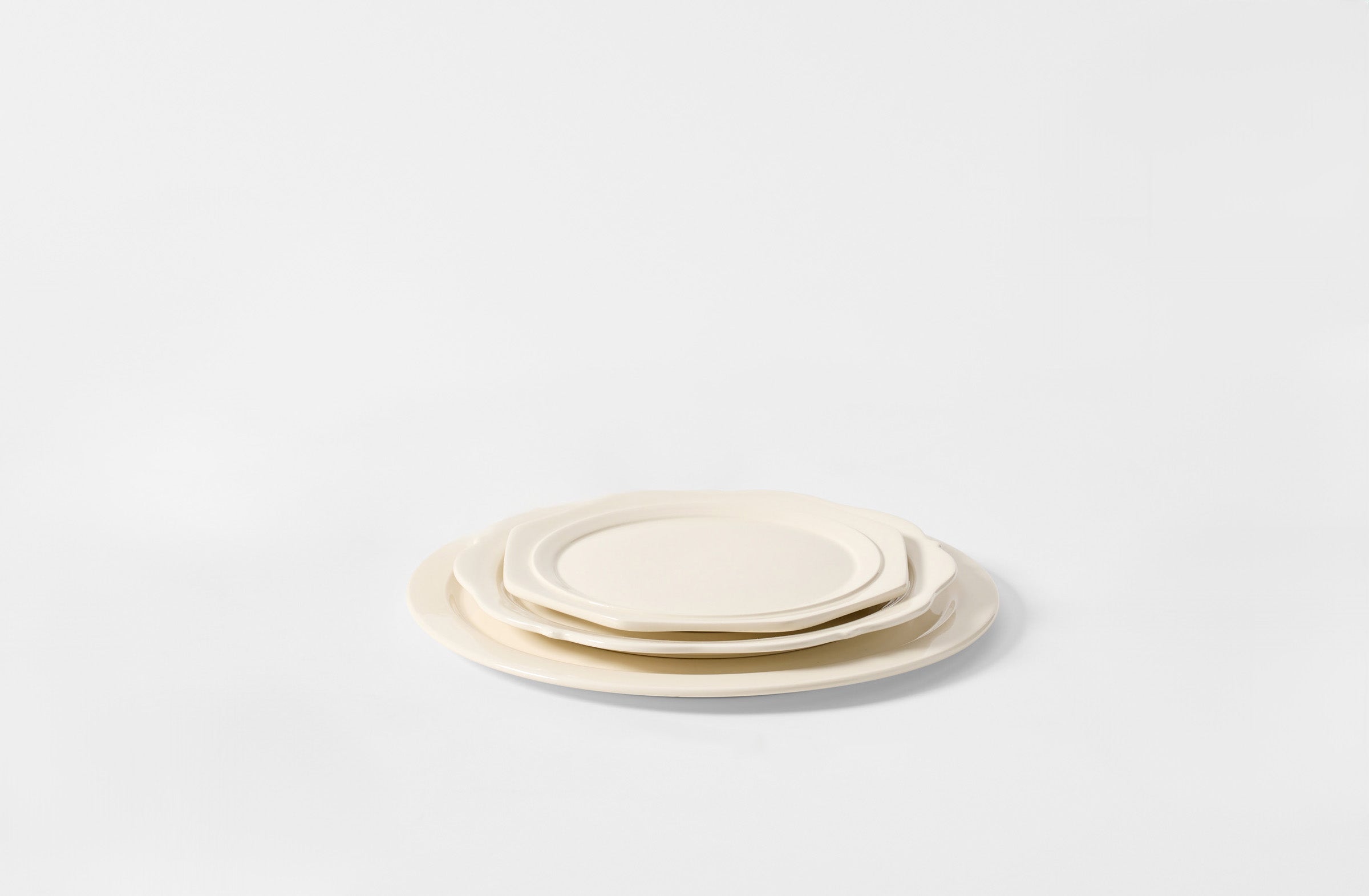 Set of three cream-colored ceramic plates on a light gray background. Default