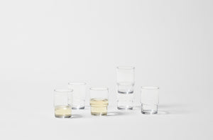 Six glass stacking tumblers a few filled with white wine on white background.