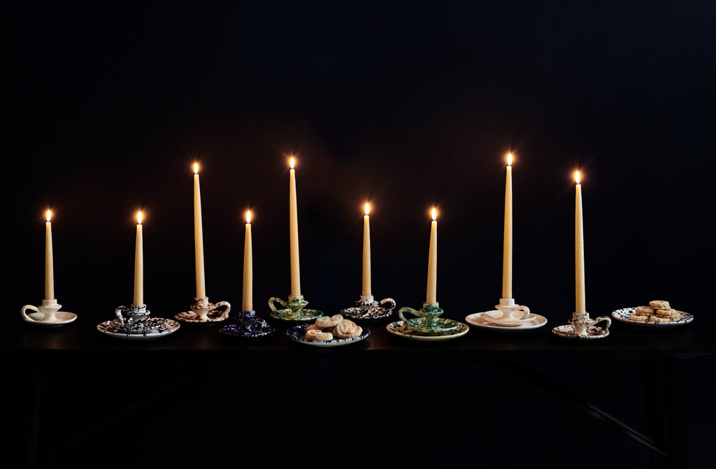 Multicolored splatterware candleholders with lit taper candles enmasse against a dark background