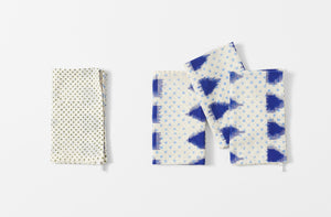 four folded gregory parkinson indigo triangle napkins with one napkin folded to the reverse pattern