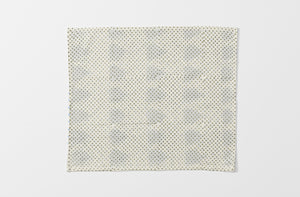 one unfolded gregory parkinson indigo triangle napkin showing the reverse patter of small khaki dots on cream