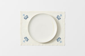 malaika ottoman blue on cream embroidered placemat shown from overhead set with a white dinner plate