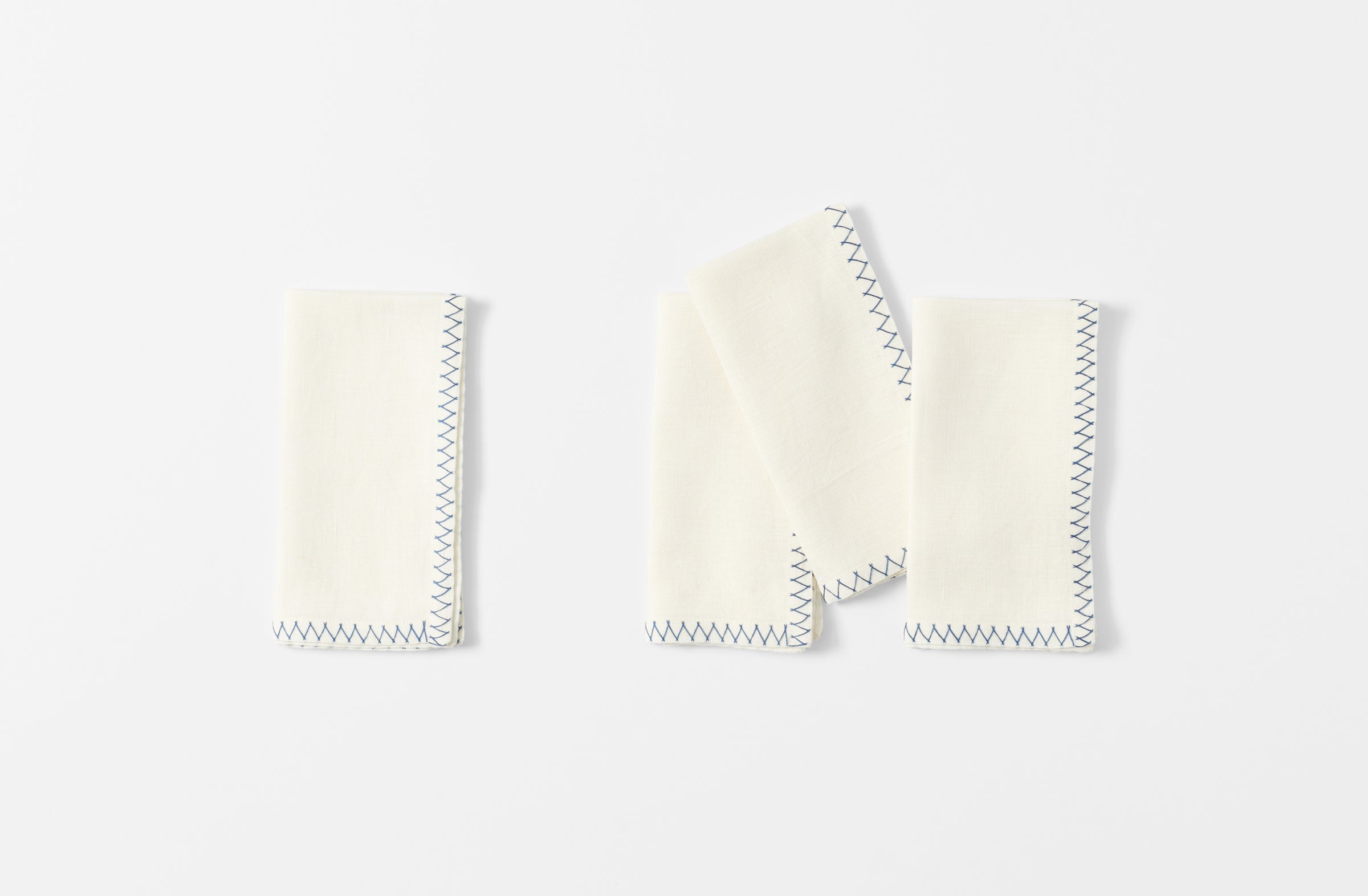 four white malaika napkins with a zig zag blue hand embroidered edge shown folded