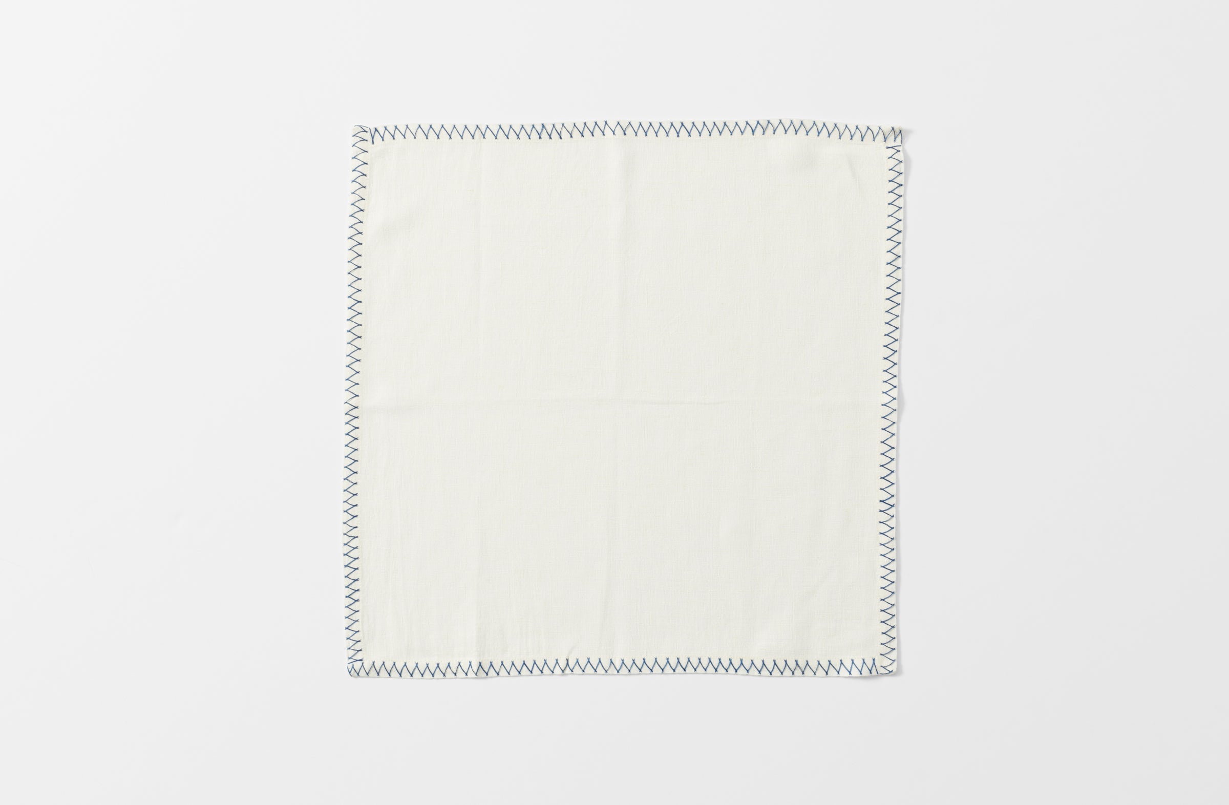 one white malaika napkin with a zig zag blue hand embroidered edge shown unfolded from above