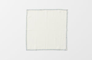 one white malaika napkin with a zig zag blue hand embroidered edge shown unfolded from above