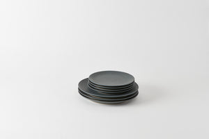Stack of slate Christiane Perrochon ceramic plates on a white background. Default