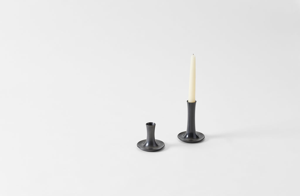 Two oxidized bronze candle holders with a white candle on a light gray background. default 