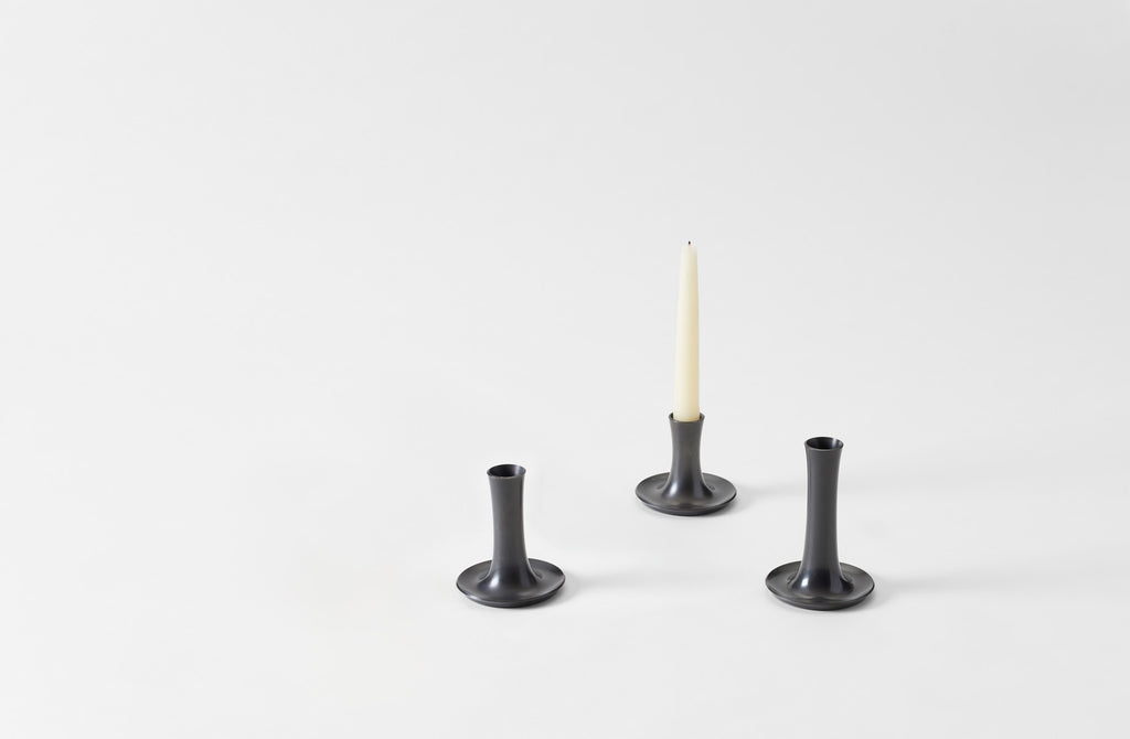 Three oxidized bronze candle holders with a white candle on a light gray background. Default 