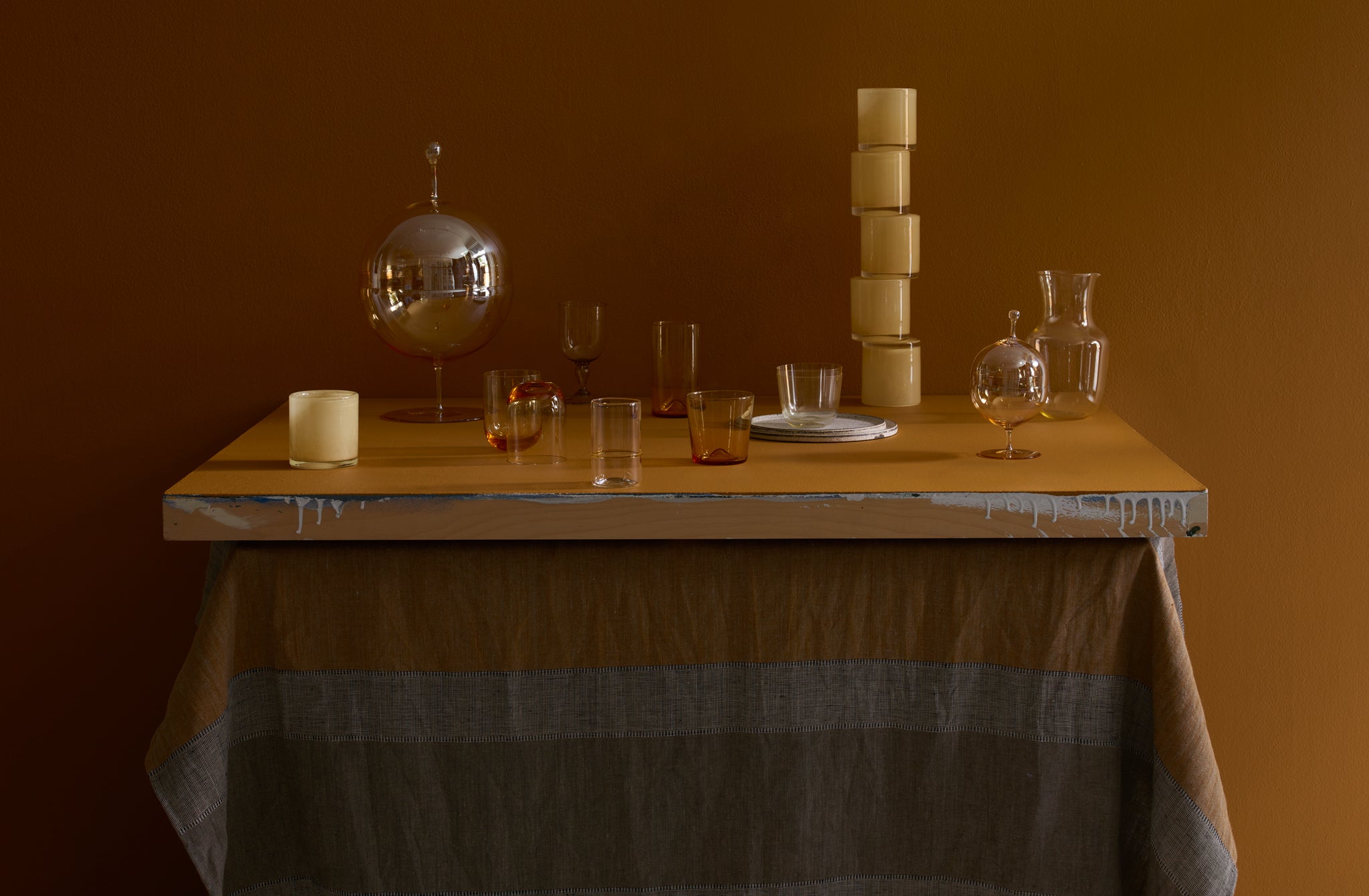 An arrangement of amber gold and straw colored Lobmeyr and Henry Dean glass on tabletop with butternut stripe tablecloth.