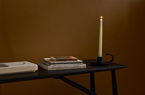 BCMT Co Cast Iron Candlestick creates warmth at the end of the Sawkille Penn console with a lit candle a small stack of vintage books and a Michael Verheyden marble tray against a dark bronze wall.