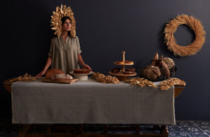 Woman at antique table wearing woven straw headdress surrounded by bread and Kelly Wearstler serving pieces.