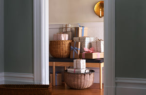 A peek through a doorway at an abundance of wrapped gifts in Jonathan Klein baskets on the Bowen Liu Feast Ash and Black Leather Bench below a Malin Appelgren Large Brass Sconce. 