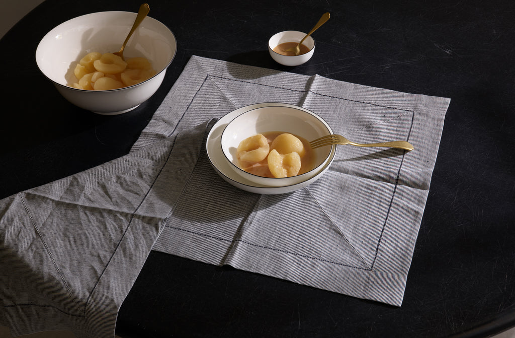 Blackline dinnerware and serving bowls from Richard Brendon set for a single serving of poached pears with Dolcevita gold flatware atop a Peter Speliopoulos navy ticking stripe linen napkin.