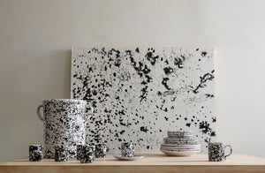 Arrangement of black on white MARCH splatterware on table against a splattered black on white canvas. Default