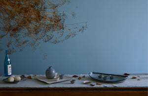 Table set for winter sake with Christiane Perrochon long oval dish and trays holding iron blue sake bottle and cups on top of pale blue fringed runner.