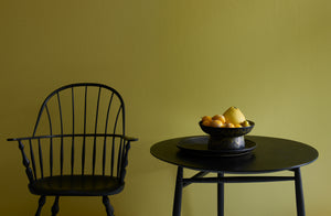 Sawyer Made black ebonized wooden sack back windsor armchair and spindle table from Sawkille Co against a gold green wall with Christiane Perrochon black ochre spot centerpiece vase and round platter.