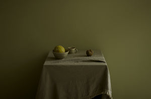 Soft light on green monochromatic scene of Christiane Perrochon green gray spot glazed bowl and mug on moss macrame edge linen tablecloth.