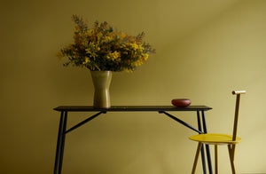 Faye TooGood Tumeric Spade Chair next to Sawkille Co. ebonized black walnut console table with Milena Kling medium chestnut glass vessel and a Christiane Perrochon yellow-green large hourglass vase holding a voluminous golden arrangement.