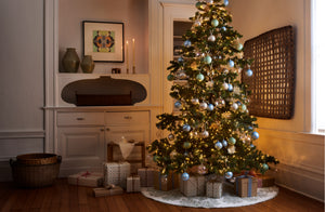 Decorated Christmas tree on MARCH Liberty print Hawaiian quilt tree skirt in softly lit room with Jonathan Kline large white tray sculpture and baskets and Christiane Perrochon  green grey spot vases.