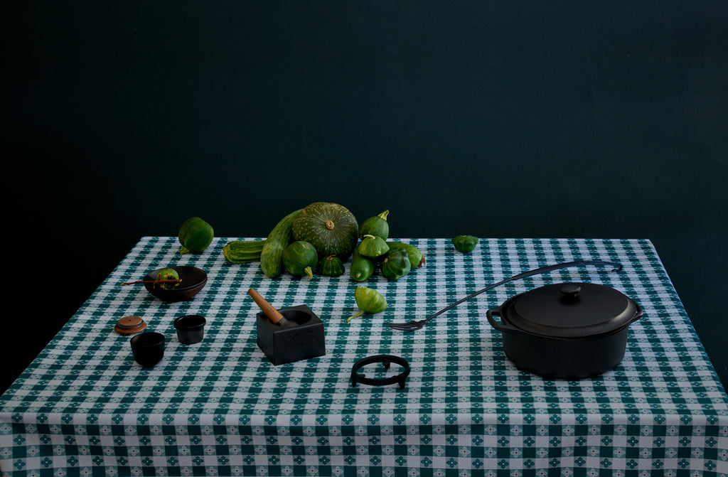 Assorted cast iron and forged steel cookware from Skeppshult Smith Shop and Blackcreek Mercantile on green patterned tablecloth with a mound of green gourds.