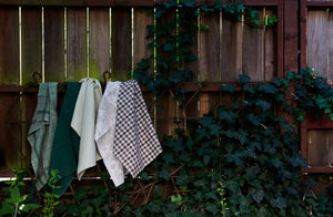 A selection of kitchen towels in mix of nuetrals and green from Charvet and Tori Murphy hanging from an ivy covered fence.