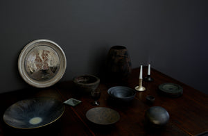 Subdued tabletop arrangement with Takashi Endo and Michaël Verheyden bowls flanked by Victoria Morris raku fired vessels with subtle silver highlights from a Karen Swami mirror Maureen Fullam antiqued silver mirror coaster and Ted Muehling silver fluted candlestick.