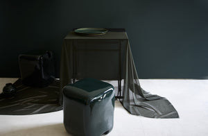 Organic and glossy green Faye Toogood cobble stools next to black Ifuji folding table drapped with ethereal sheer fabric and holding shiny spruce green Christiane Perrochon platter.