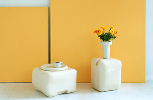 faye-toogood-cream-cobble-furniture-with-cream-dough-vase-set-with-marigold-flowers-against-marigold-background