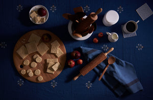 Holiday cookies with folk rolling pin on blue ottoman vase tablecloth and wooden utensils.