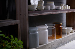 Outdoor wooden shelving with stacks of MARCH cream on white splatterware and Henry Dean glass garden seats.