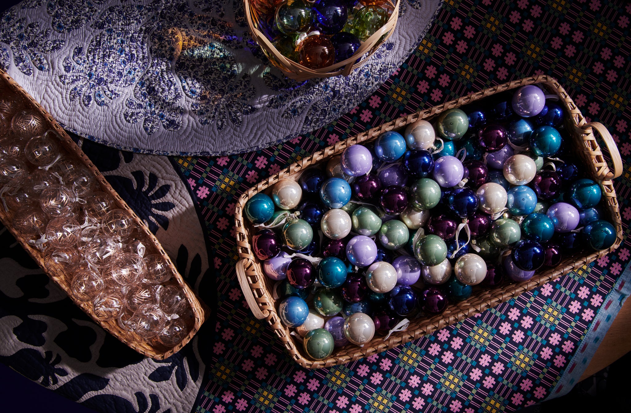 Glass holiday ornaments in baskets sitting on Hawaiian tree skirts and Gregory Parkinson night sky garden throw