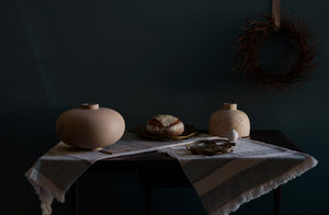 Rustic wreath hanging above arrangement of Joshua Vogel sculptures celtic knot baskets and tiny Takashi Endo vase sitting on folded diamond edge linen tablecloth.