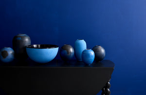 Smoke fired blue and cobalt Karen Swami vessels on table against an indigo wall.Smoke fired blue and cobalt Karen Swami vessels on table against an indigo wall.