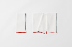 Four folded red edge white linen napkins.