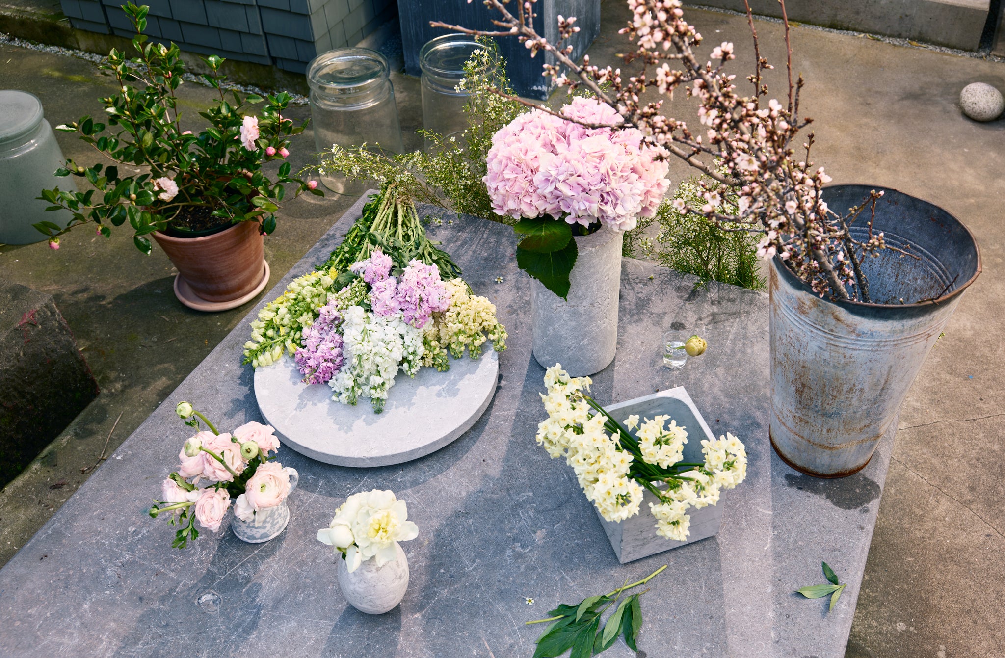 Blue stone garden table set with Michaël Verheyden grey marble vases and platter filled with spring pastel flowers.