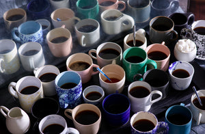 variety of mixed hand made mugs in different colors and shapes set enmasse on a tray filled with coffee
