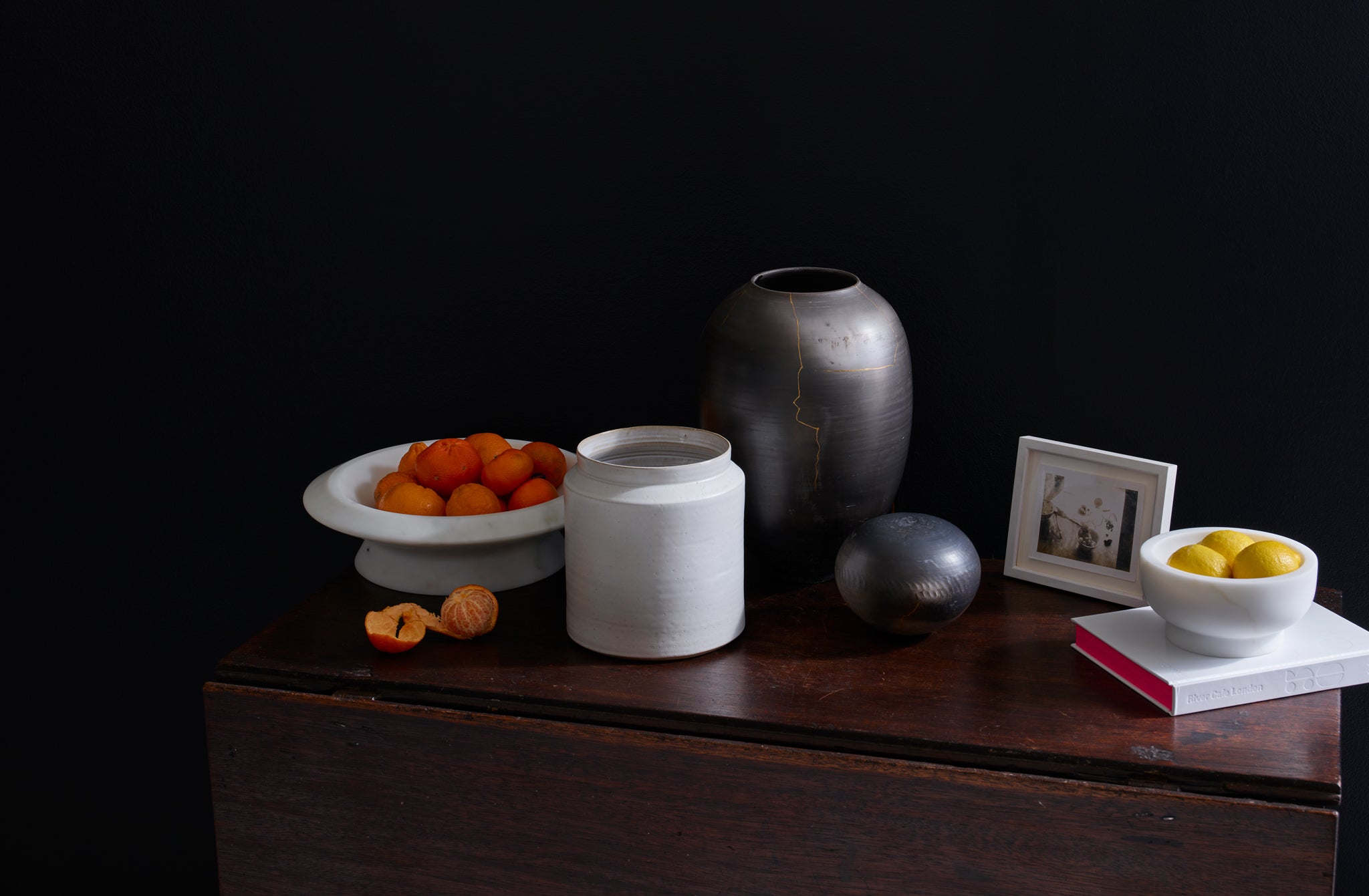 Marble bowls filled with citrus, Karen Swami ceramics, and a Traci Hervy for MARCH white utensil crock, all displayed on an antique table.