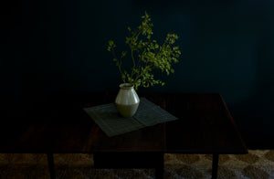 Green branches of Japanese Maple in a Christiane Perrochon green grey spot vase on top of a Peter Speliopoulos plaid napkin canopy over Antique 19th Century Mallorca Table on a jute rug.