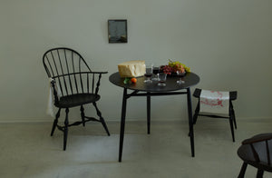 Sawkille Co. black walnut spindle table holding a part of a wheel of cheese grapes and mix of glassware with Sawyer Made Black Sack Back Armchair and Ifuji Black New R Chair under small Maureen Fullam mirror.