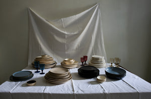 Piles of plates and bowls with Davide Fuin goblets tucked in between on patterned draped white damask featuring Brickett Davda Francis Palmer Anita Le Grelle and Le Mere Ebony dinnerware.