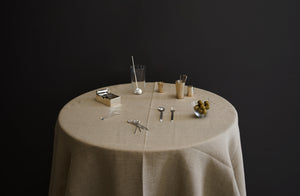 A round table dressed with Peter Speliopoulos natural linen tablecloth with steling silver barware and serveware from Heath Wagoner and John Corcoran and Deborah Ehrlich glass bowl holding large green olives.