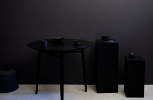 Dark Moody image of Takashi Endo black ceramics stacked on ebonized wood plinths and a Sawkille ebonized spindle table in a gallery setting.