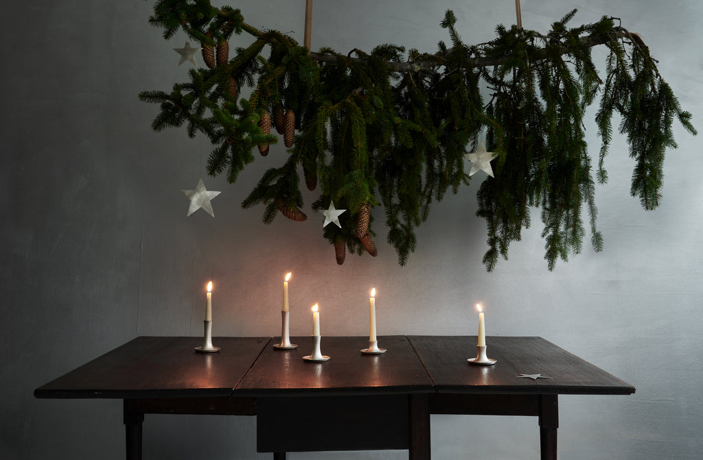 Hanging greenery above a wooden table with lit candles against a gray wall. Default