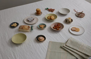 A spread of holiday cookies in small bowls and on tiny plates by Christiane Perrochon Brickett Davda Richard Brendon and Takashi Endo with softly folded celadon and off white stripe napkins.